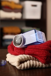 Modern fabric shaver and knitted clothes on wooden table indoors, closeup. Space for text
