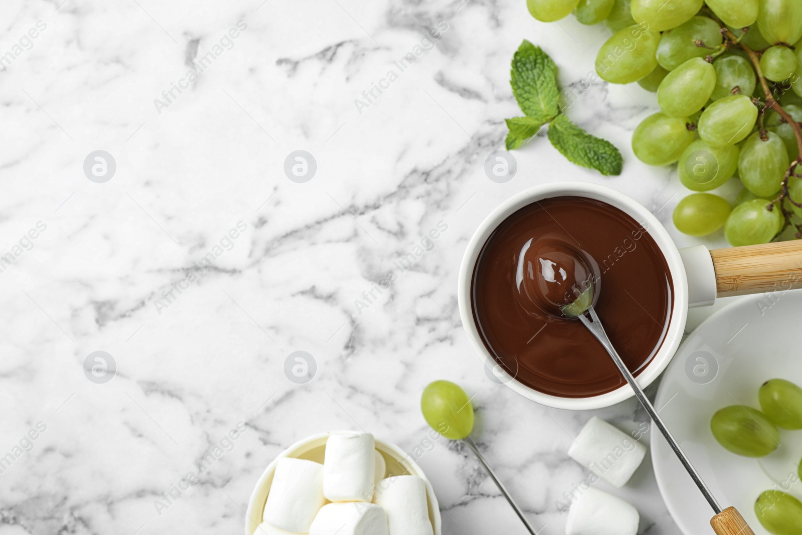 Photo of Dipping grape into fondue pot with dark chocolate on marble table, top view. Space for text