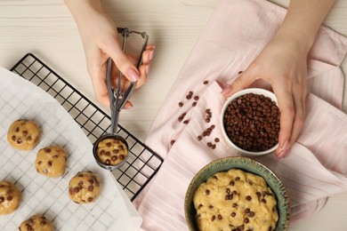 Photo of Woman making delicious chocolate chip cookies at white wooden table, top view