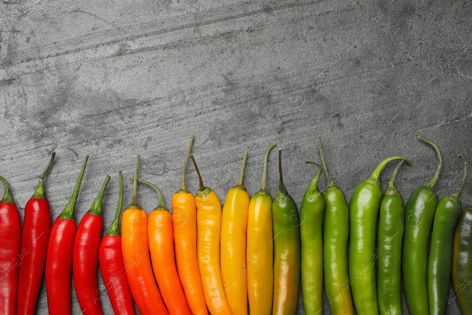 Photo of Different ripe chili peppers grey table, flat lay. Space for text