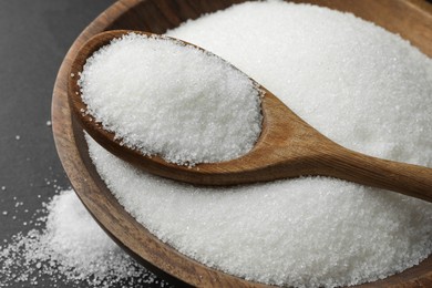 Granulated sugar in bowl and spoon on black table, closeup