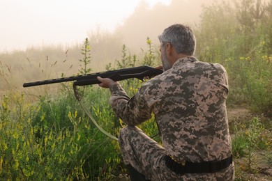 Man wearing camouflage and aiming with hunting rifle outdoors, back view