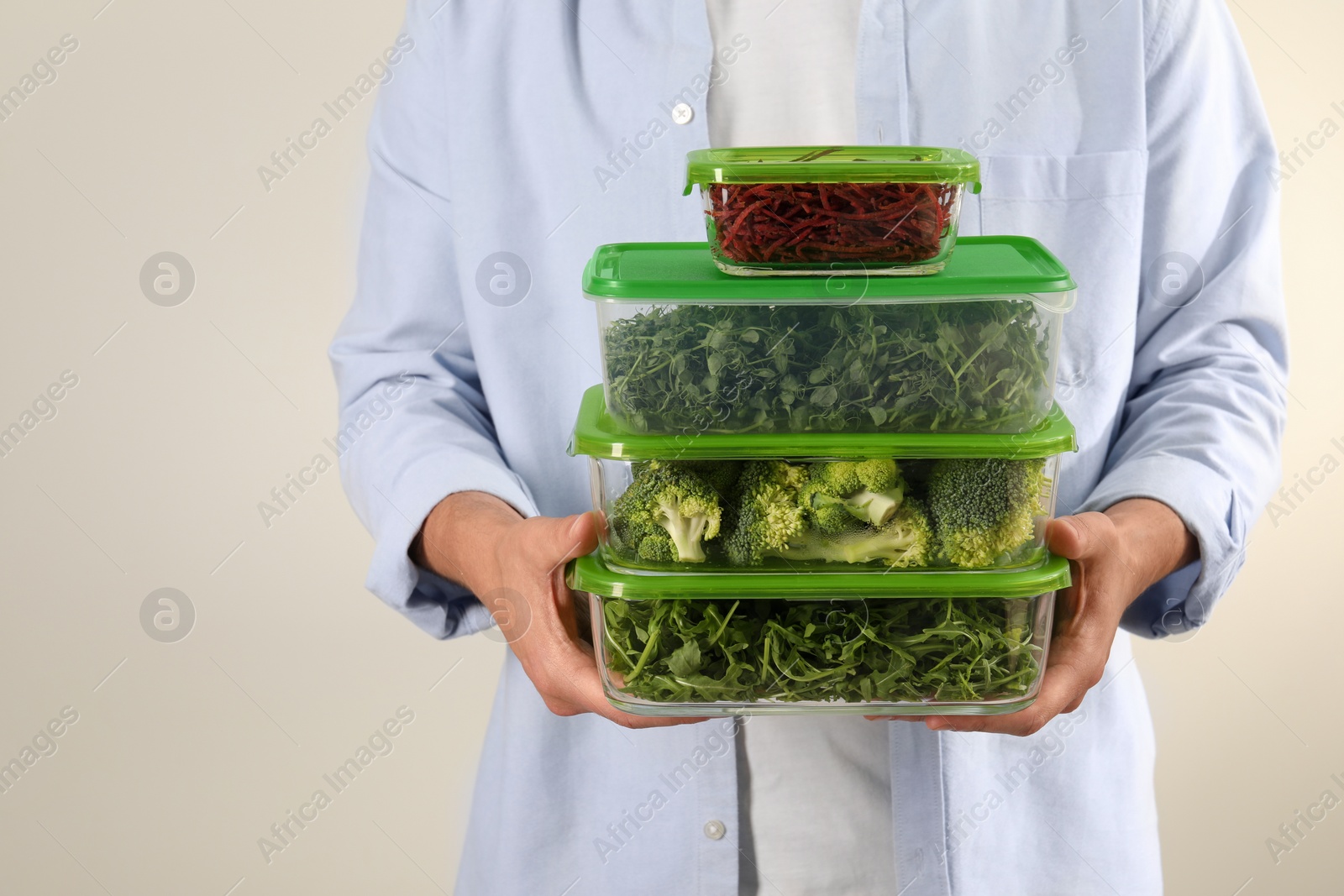 Photo of Man holding glass containers with fresh products on light grey background, closeup