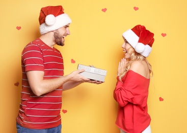Young couple in Santa hats with Christmas gift on color background