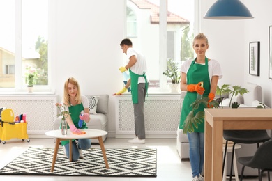 Photo of Team of professional janitors in uniform cleaning living room