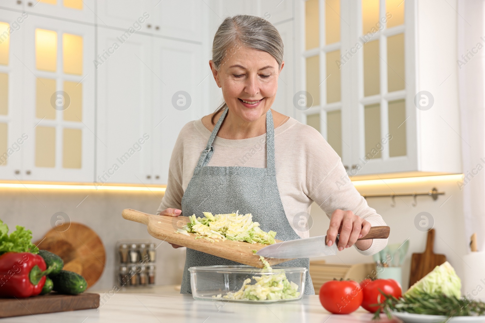Photo of Happy housewife putting cut cabbage into glass container at white marble table in kitchen