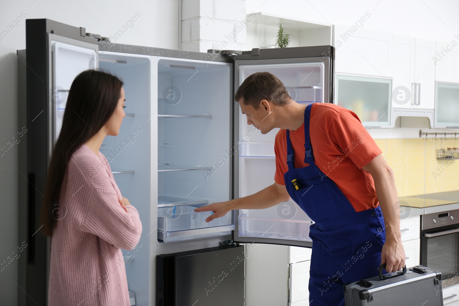 Photo of Male technician talking with client near refrigerator in kitchen