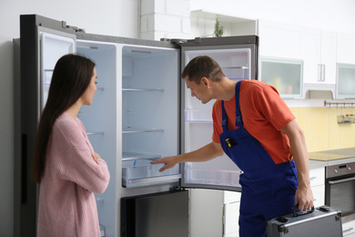 Photo of Male technician talking with client near refrigerator in kitchen