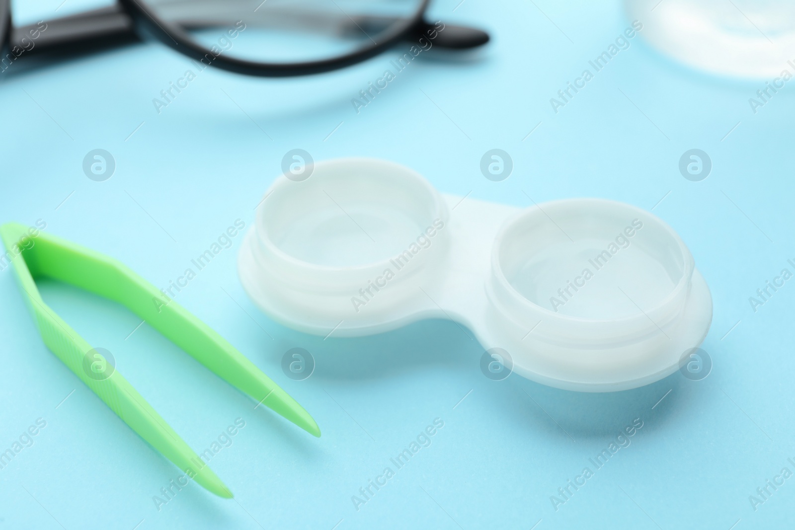 Photo of Case with contact lenses and tweezers on light blue background, closeup