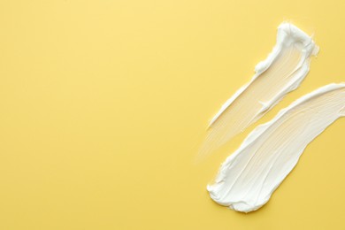 Photo of Samples of face cream on yellow background, top view. Space for text