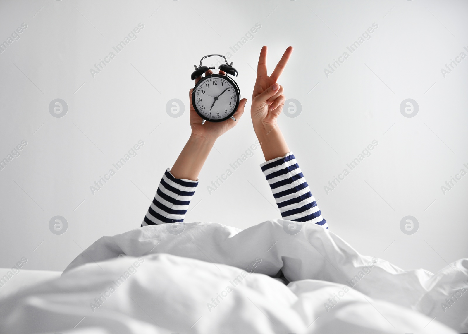 Photo of Woman with alarm clock lying in bed, closeup. Morning time