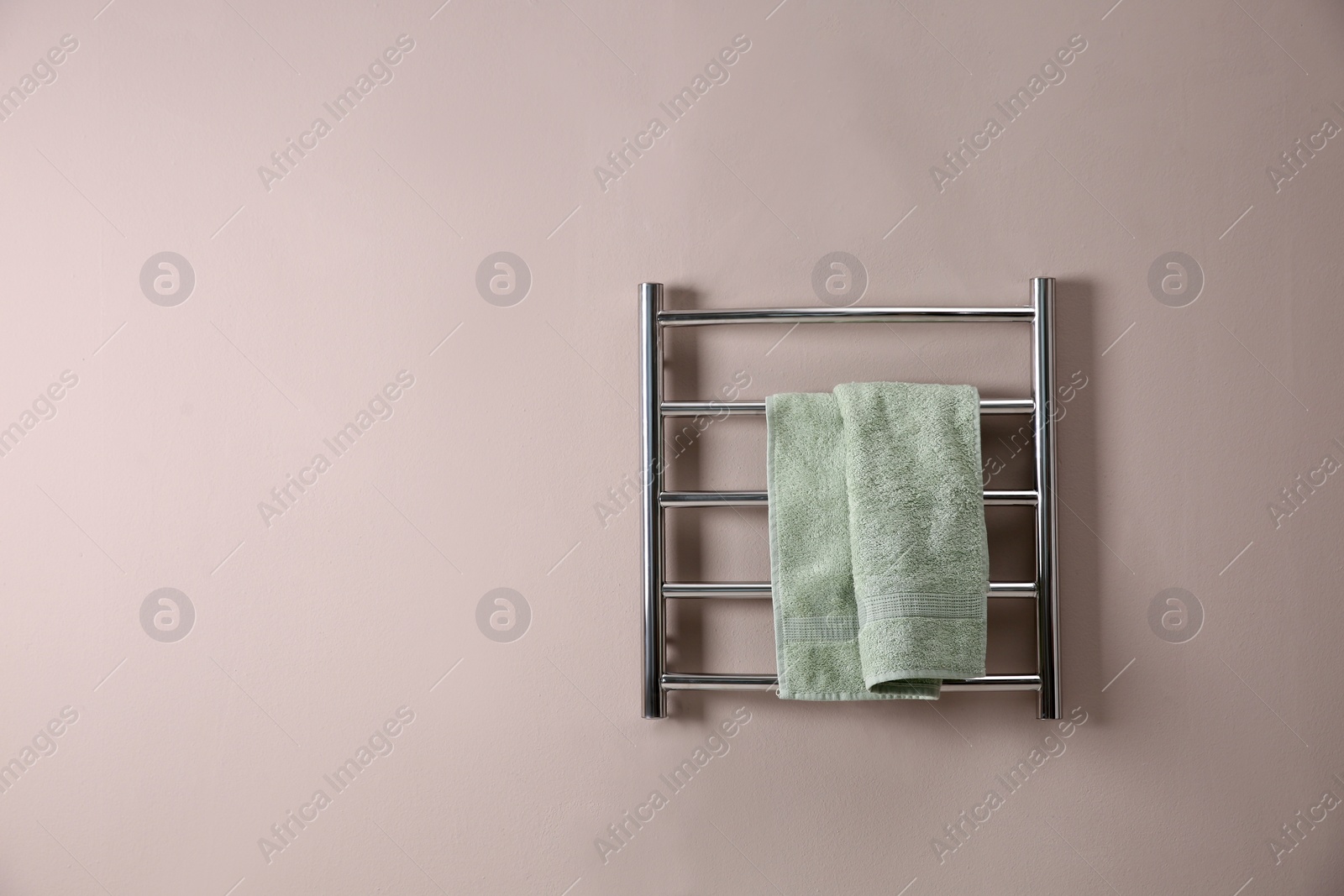 Photo of Modern heated towel rail with warm soft towel on light wall. Space for text