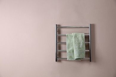 Modern heated towel rail with warm soft towel on light wall. Space for text