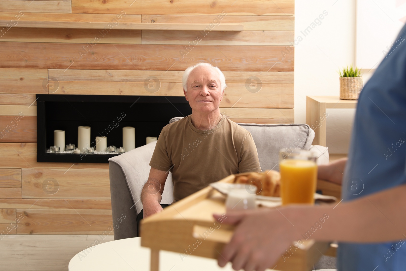 Photo of Nurse serving breakfast to elderly man indoors. Assisting senior people