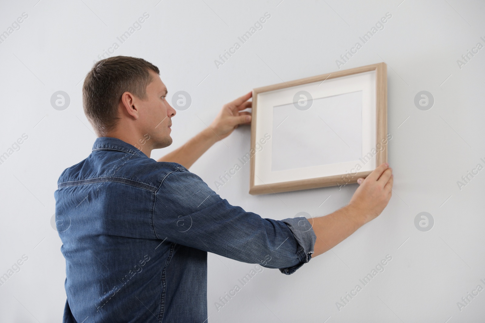 Photo of Man hanging picture on white wall indoors. Interior decoration