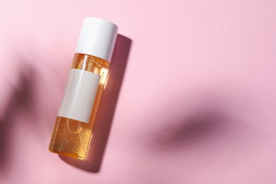 Bottle of cosmetic oil on pink background, top view. Space for text
