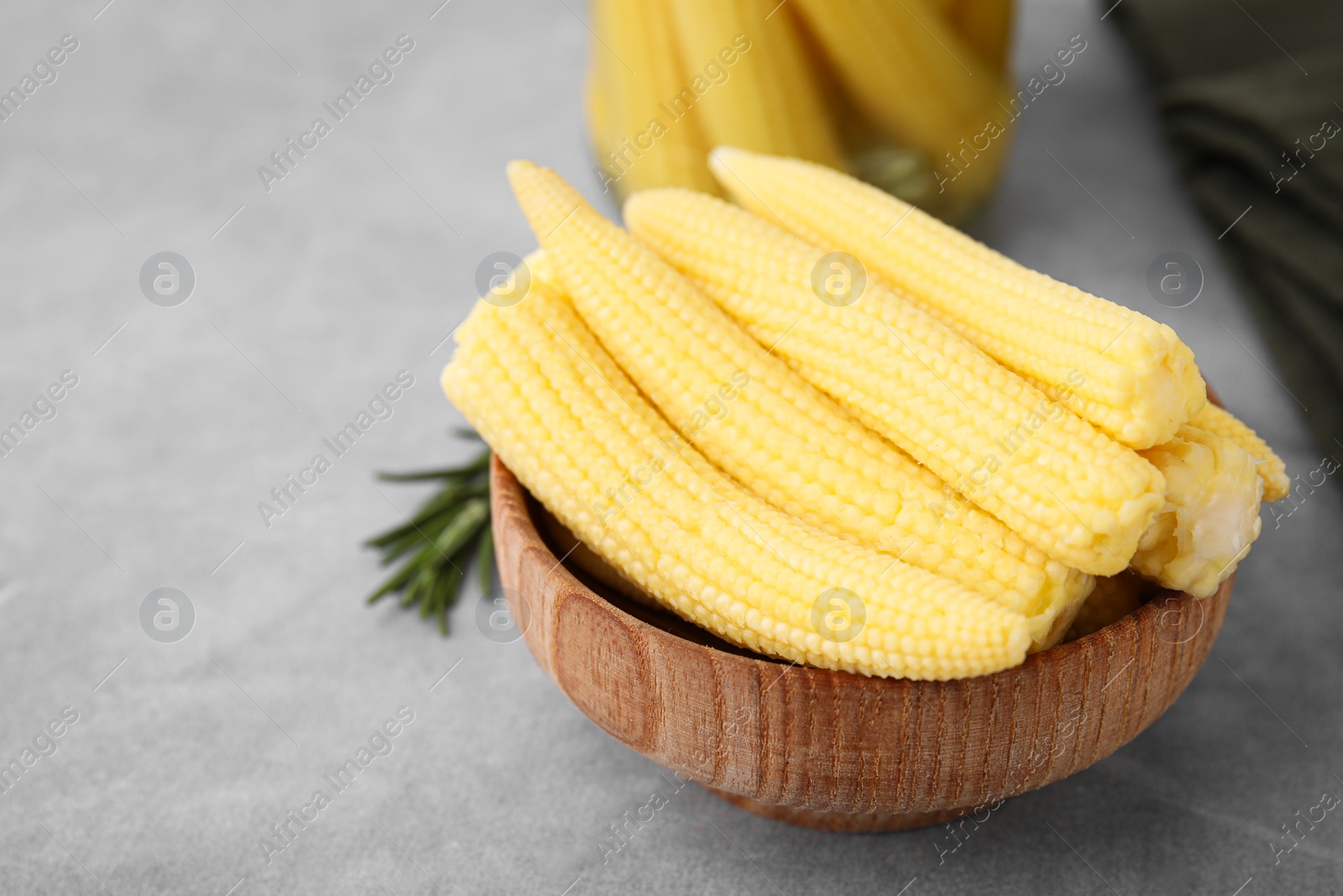 Photo of Tasty fresh yellow baby corns in bowl on grey table, space for text