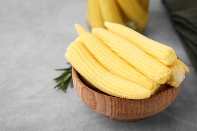 Tasty fresh yellow baby corns in bowl on grey table, space for text