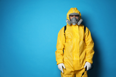 Photo of Man wearing protective suit with insecticide sprayer on blue background, space for text. Pest control
