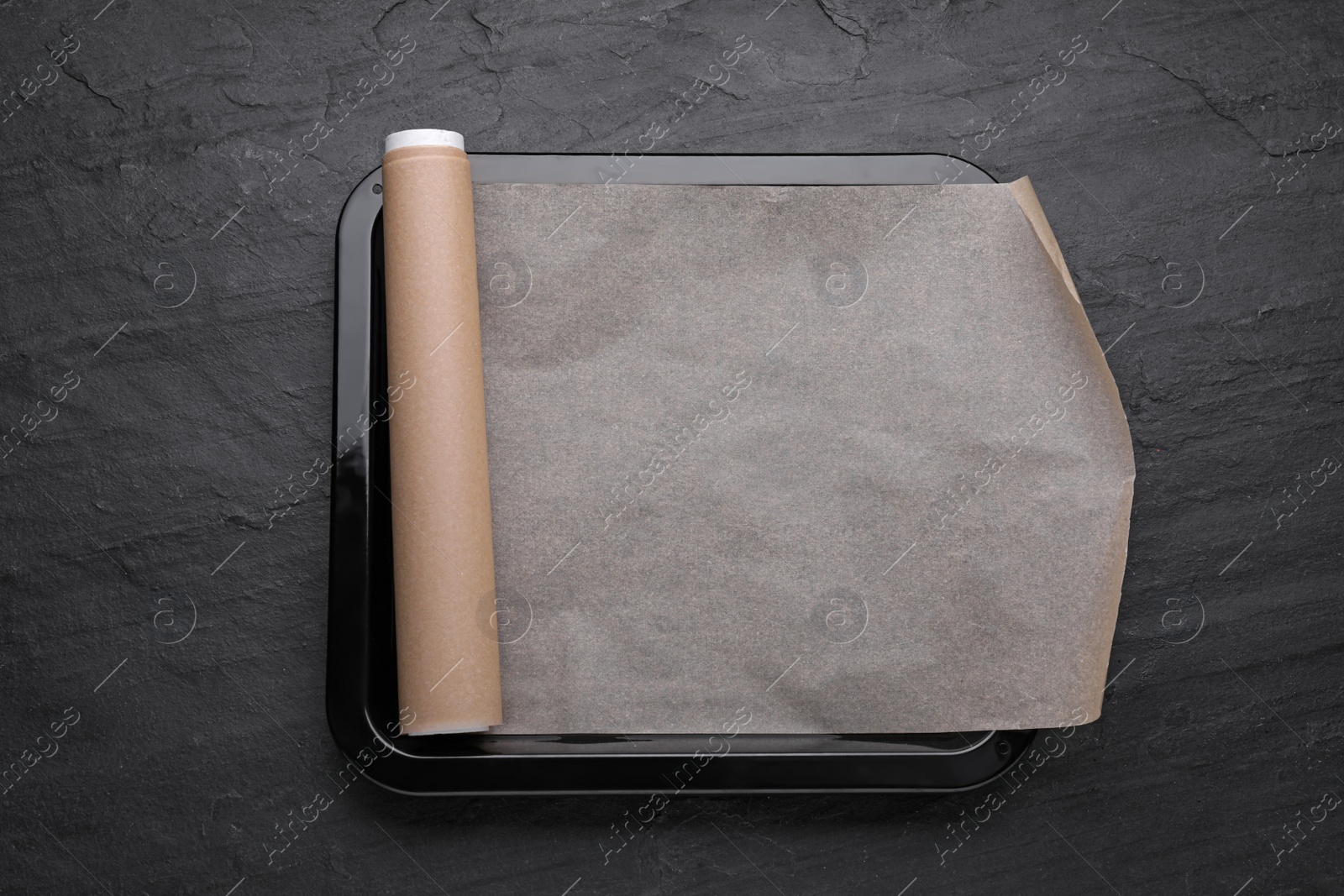 Photo of Baking pan with parchment paper on black slate background, top view