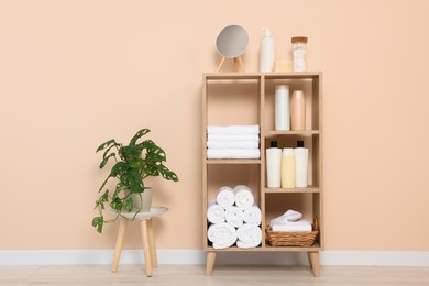 Photo of Soft folded towels and cosmetic bottles on wooden shelving unit near beige wall