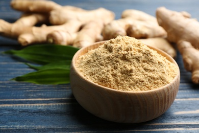 Photo of Dry ginger powder in bowl and fresh root on blue wooden table