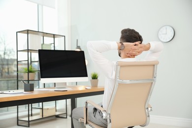 Photo of Young businessman relaxing in office chair at workplace, back view. Space for text