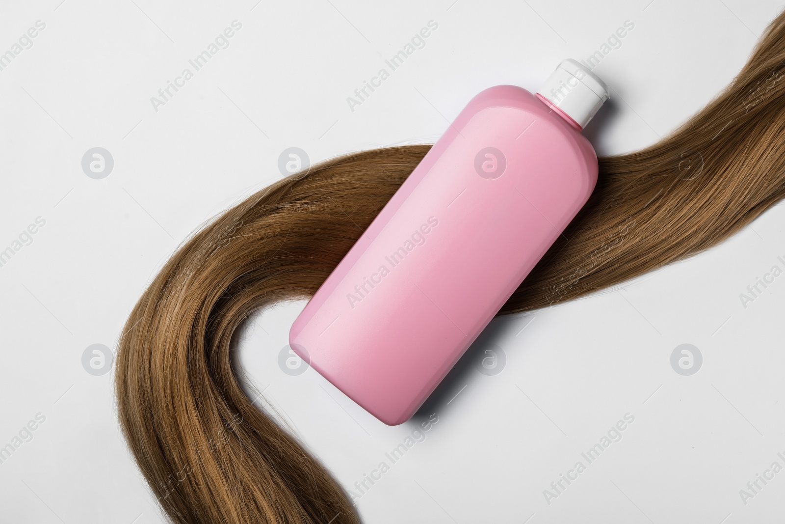 Photo of Blank bottle of cosmetic product and hair on white background, top view. Space for design