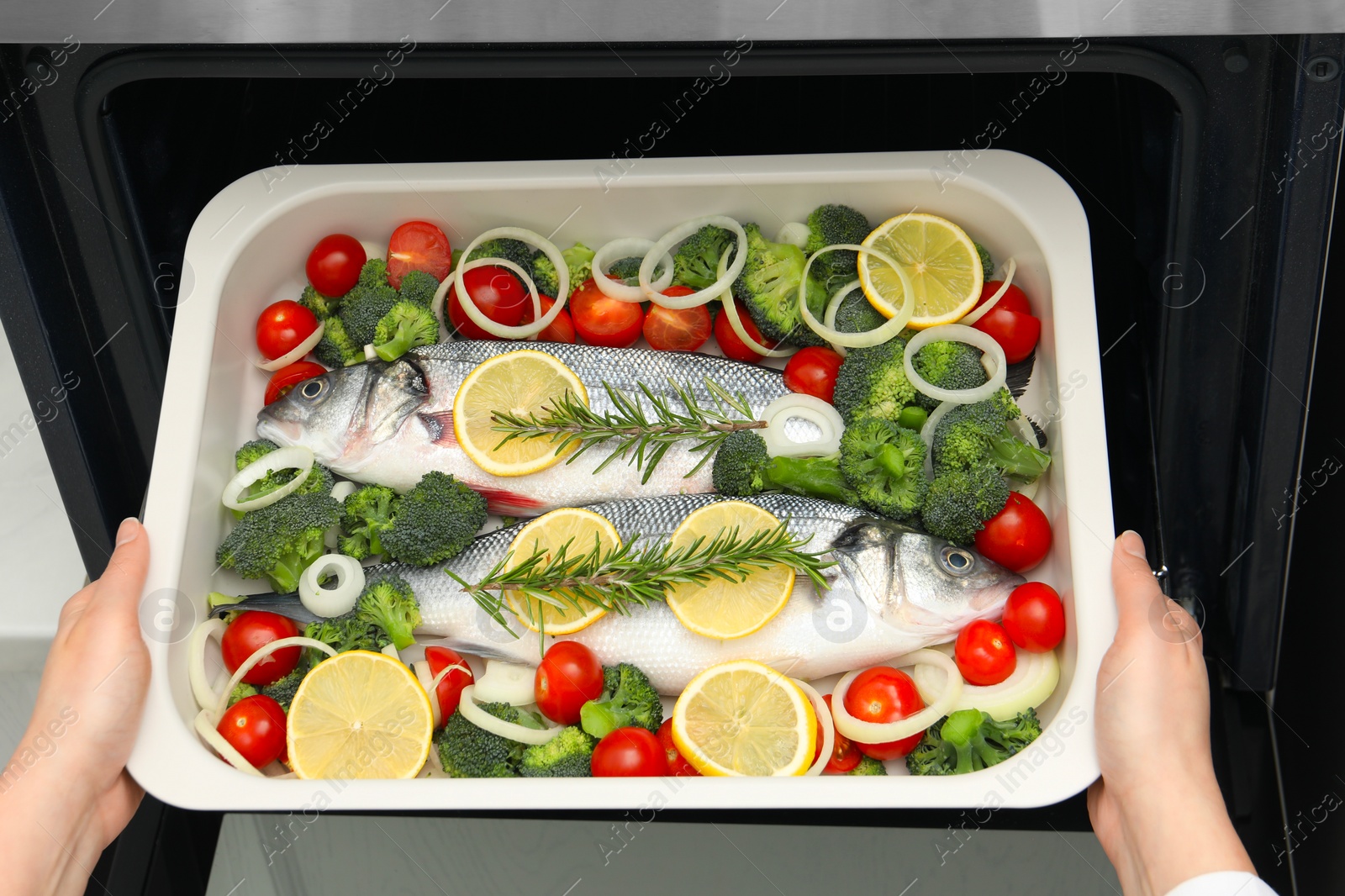 Photo of Woman putting baking dish with raw fish and vegetables into oven, top view