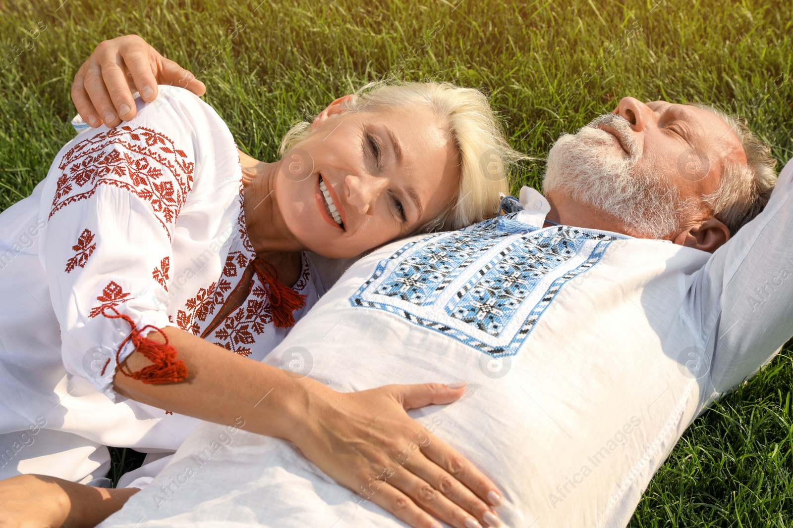 Photo of Happy mature couple in Ukrainian national clothes resting on green grass outdoors