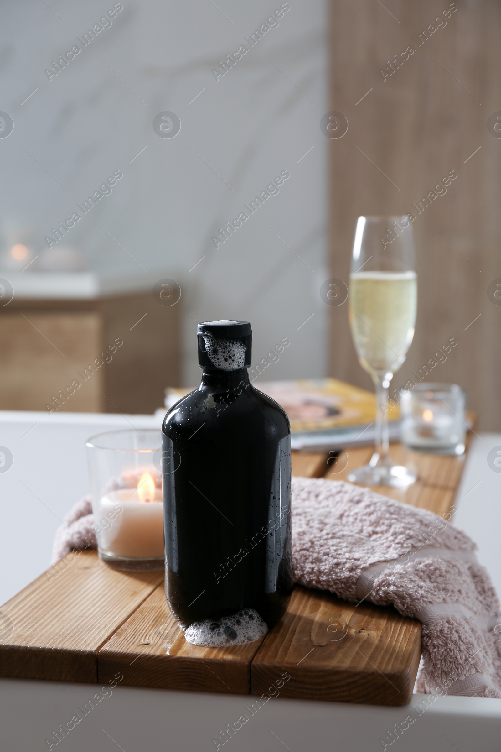 Photo of Wooden bath tray with shower gel, candle and fresh towel on tub indoors