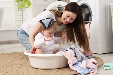 Happy mother with her daughter having fun while washing baby clothes in bathroom