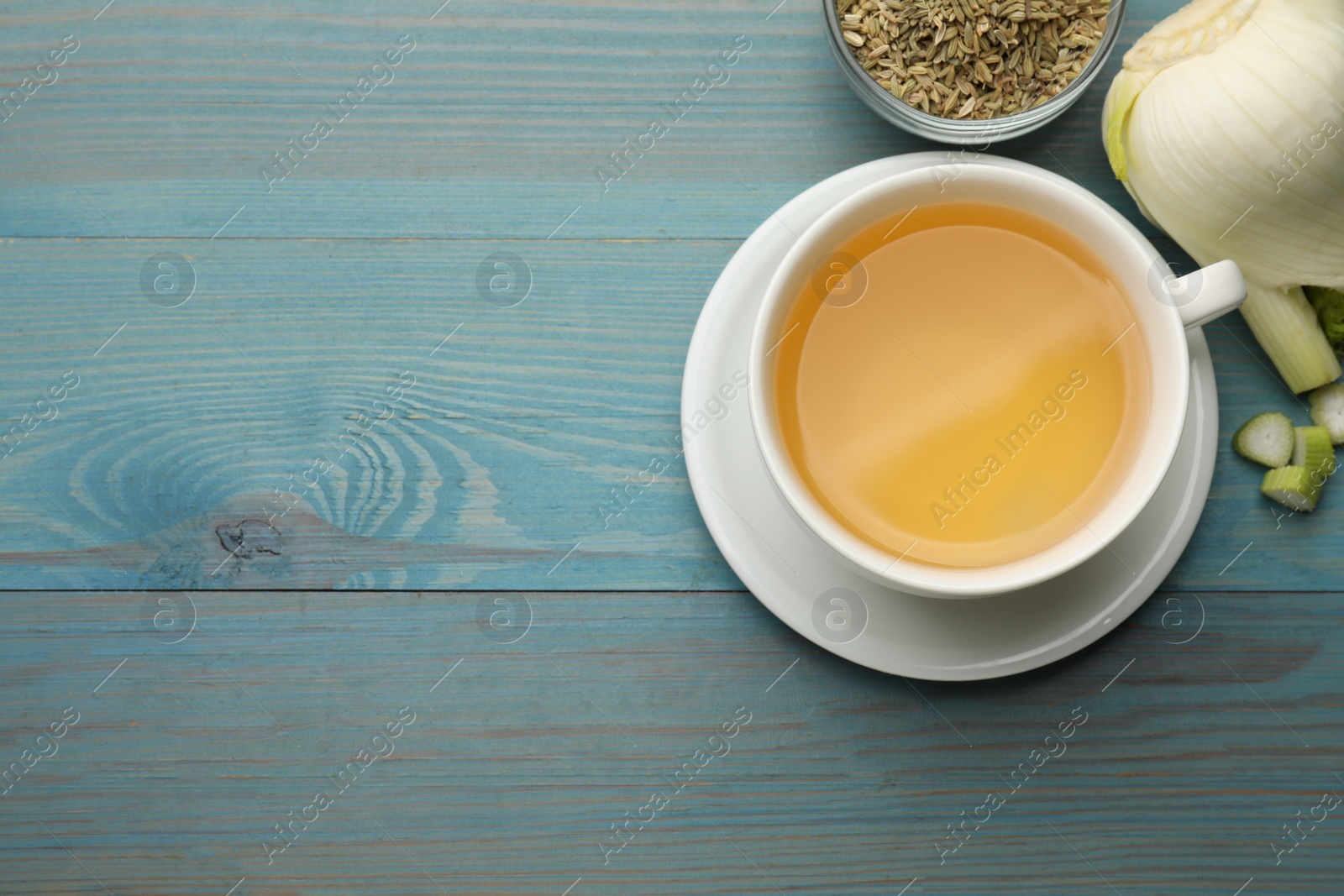 Photo of Fennel tea in cup, seeds and fresh vegetable on light blue wooden table, flat lay. Space for text