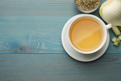 Photo of Fennel tea in cup, seeds and fresh vegetable on light blue wooden table, flat lay. Space for text