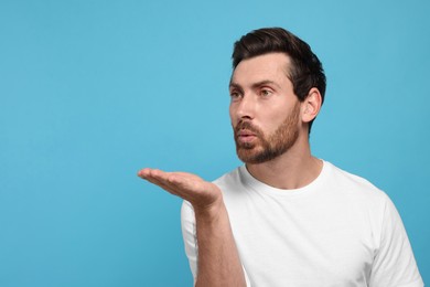 Photo of Handsome man blowing kiss on light blue background. Space for text