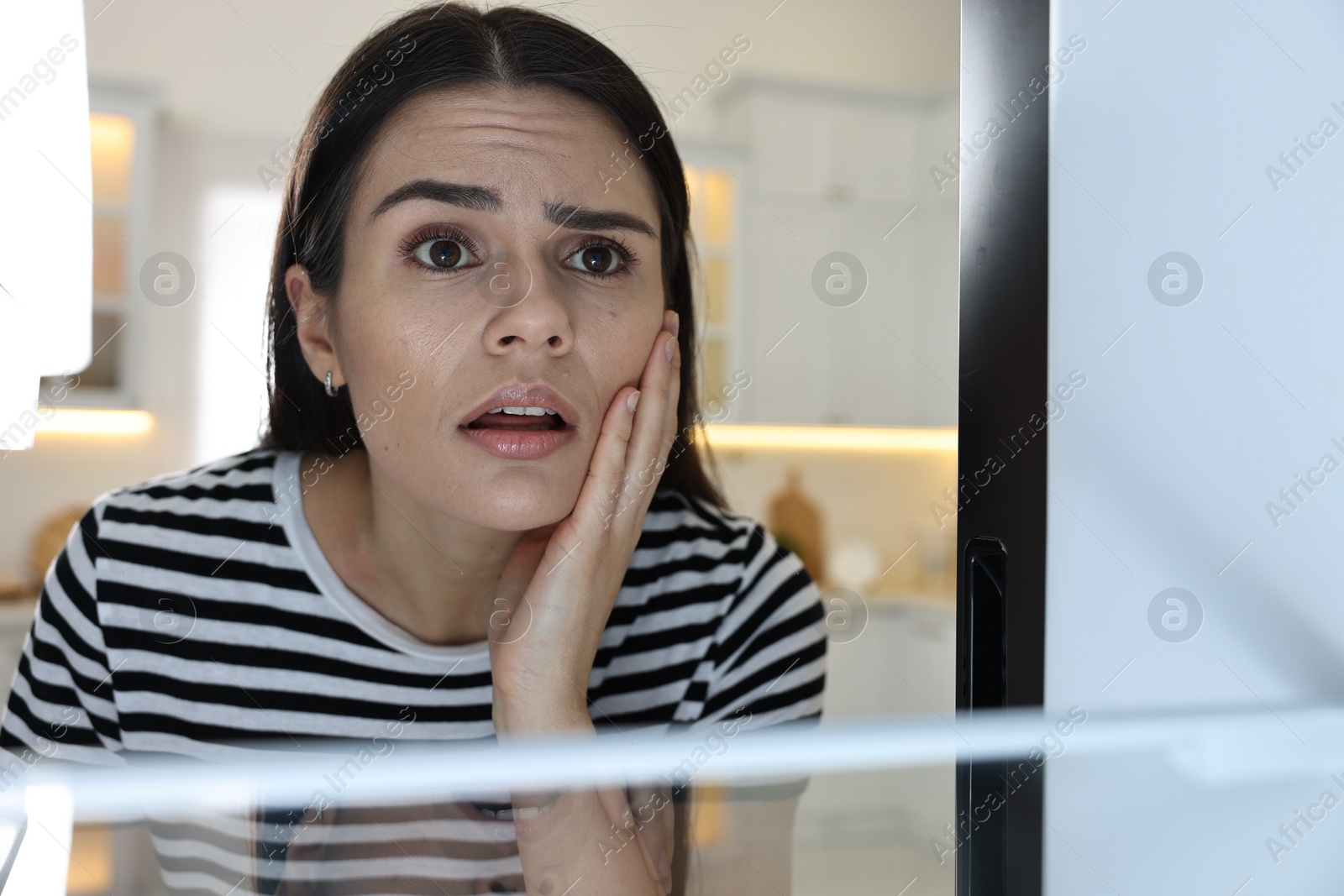 Photo of Upset woman near empty refrigerator in kitchen, view from inside