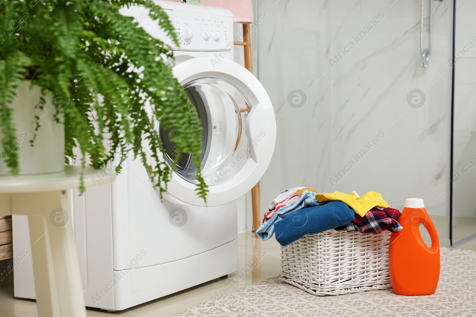 Photo of Wicker basket with laundry, detergent and washing machine in bathroom