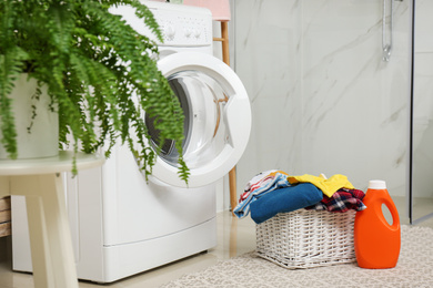 Photo of Wicker basket with laundry, detergent and washing machine in bathroom