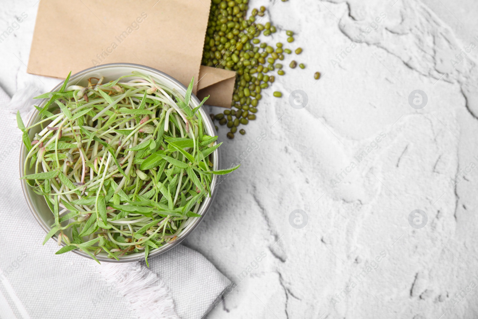 Photo of Bowl with sprouts and mung beans on white textured table, flat lay. Space for text