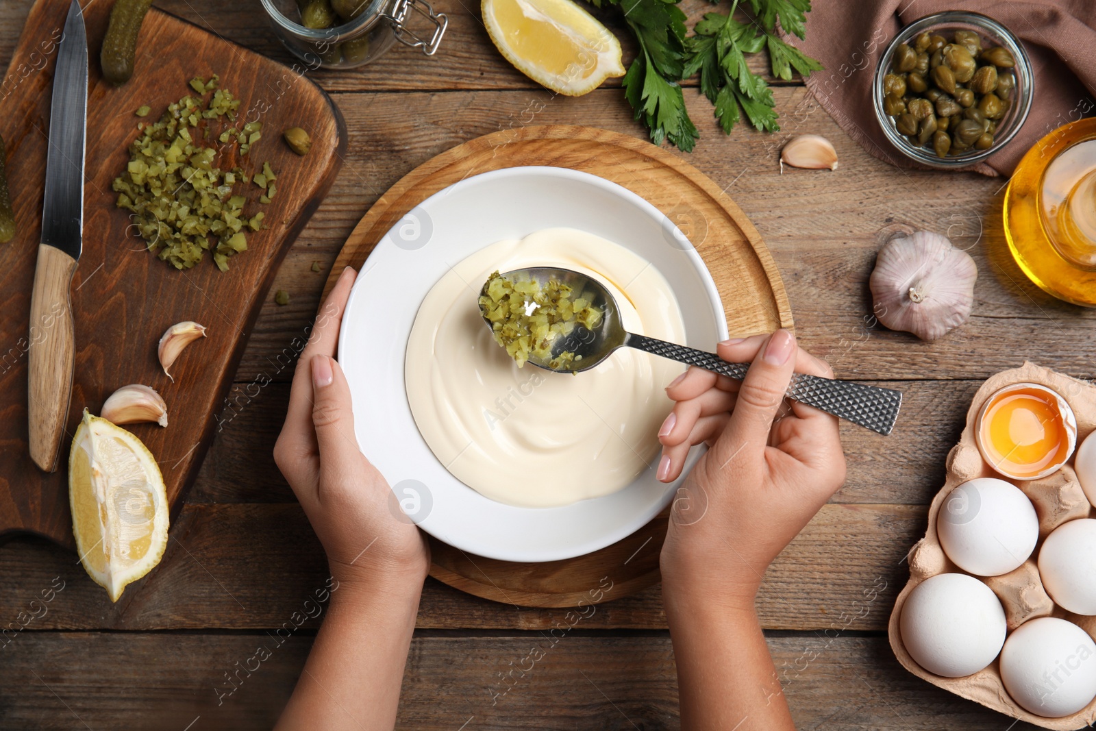 Photo of Woman making delicious tartar sauce at wooden table, top view