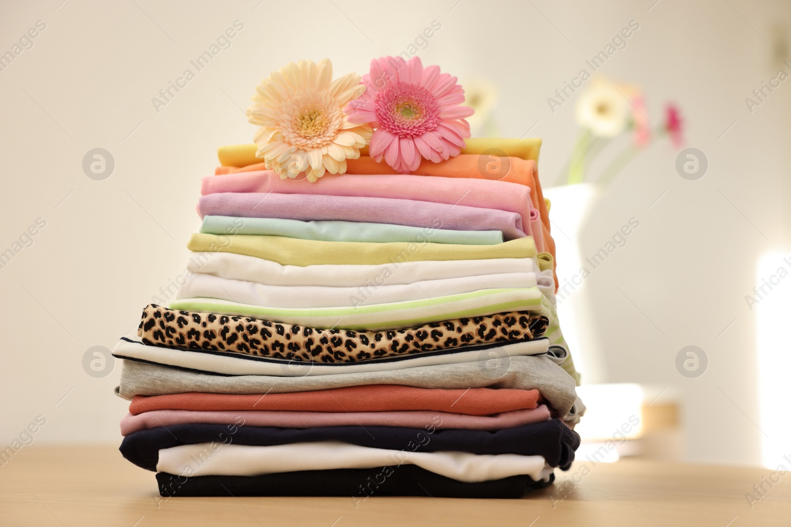 Photo of Stack of clean clothes and flowers on wooden table