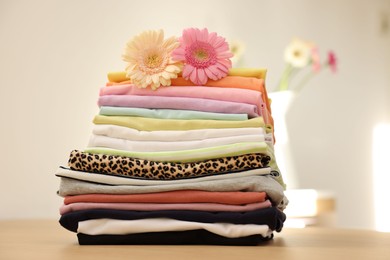 Photo of Stack of clean clothes and flowers on wooden table