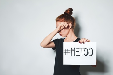 Young woman holding #METOO card against light background. Space for text