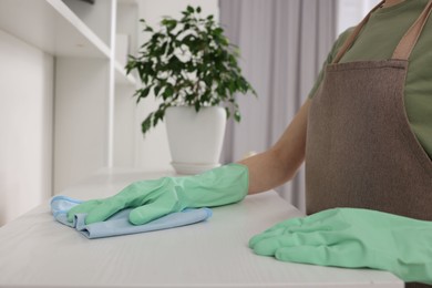 Woman with microfiber cloth cleaning white table in room, closeup