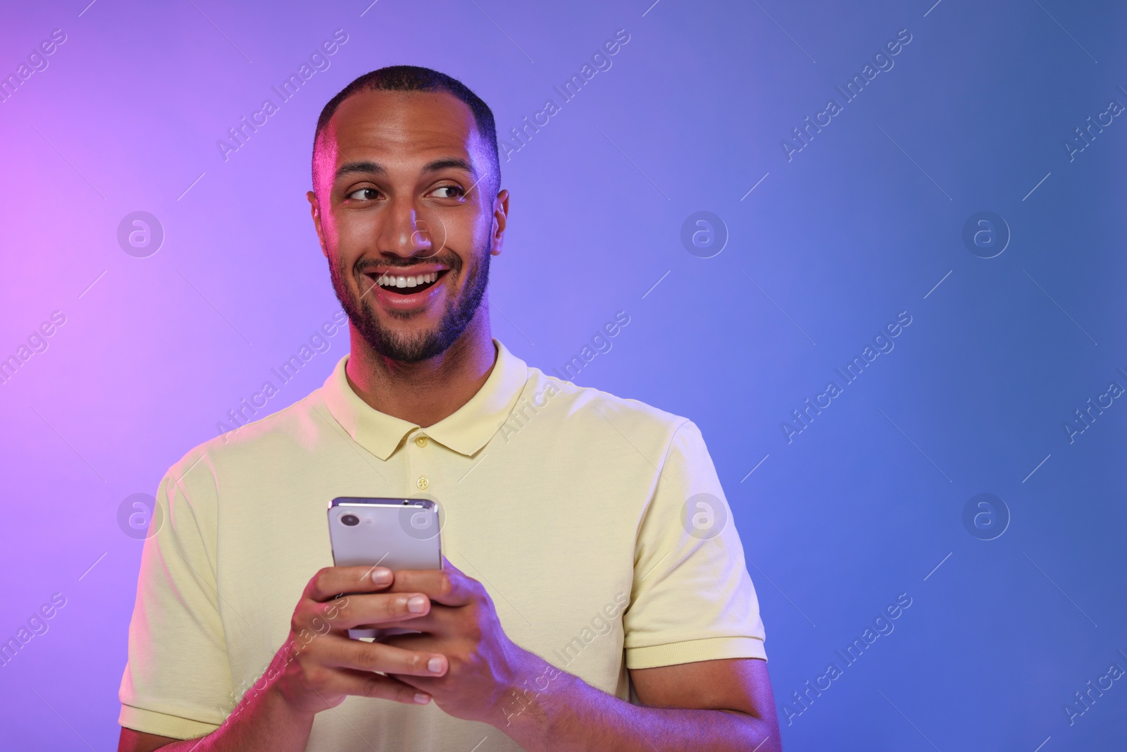 Photo of Happy man sending message via smartphone on color background, space for text