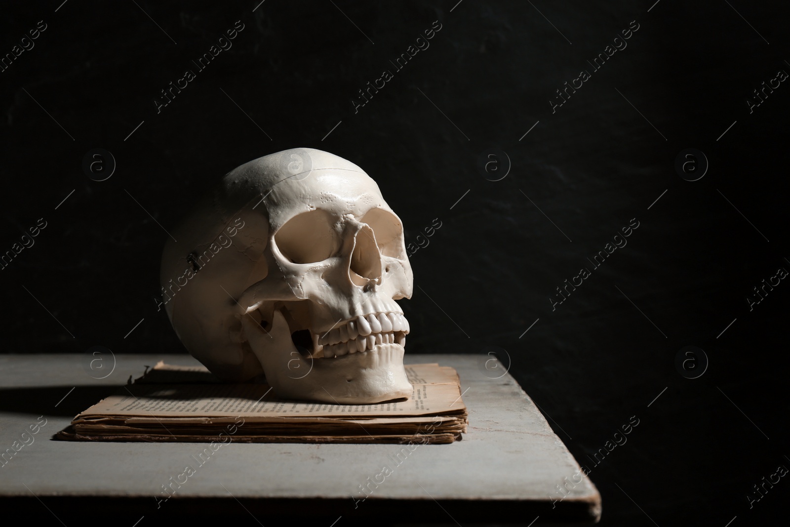 Photo of Human skull and old book on table against black background, space for text