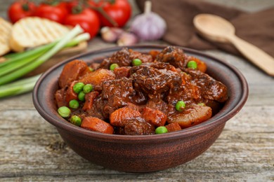 Delicious beef stew with carrots, peas and potatoes on wooden table, closeup