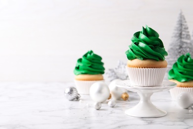 Photo of Delicious cupcakes with green cream and Christmas decor on white marble table. Space for text