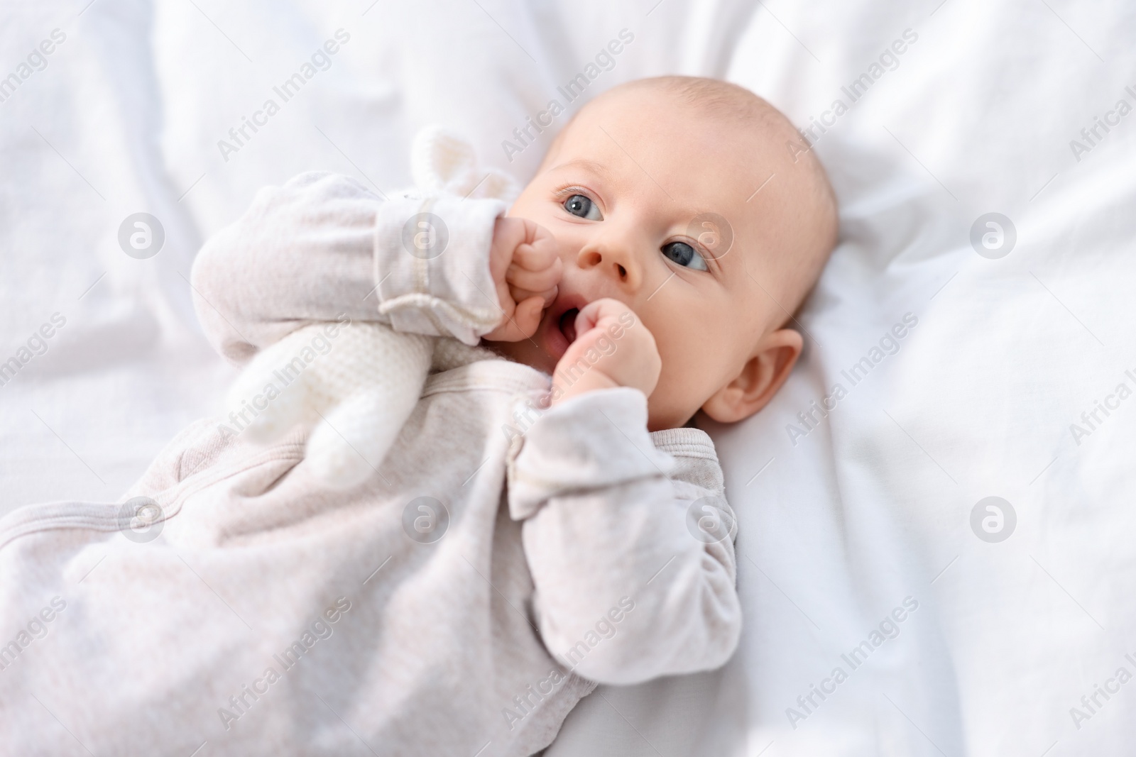 Photo of Cute little baby lying on white sheets, top view