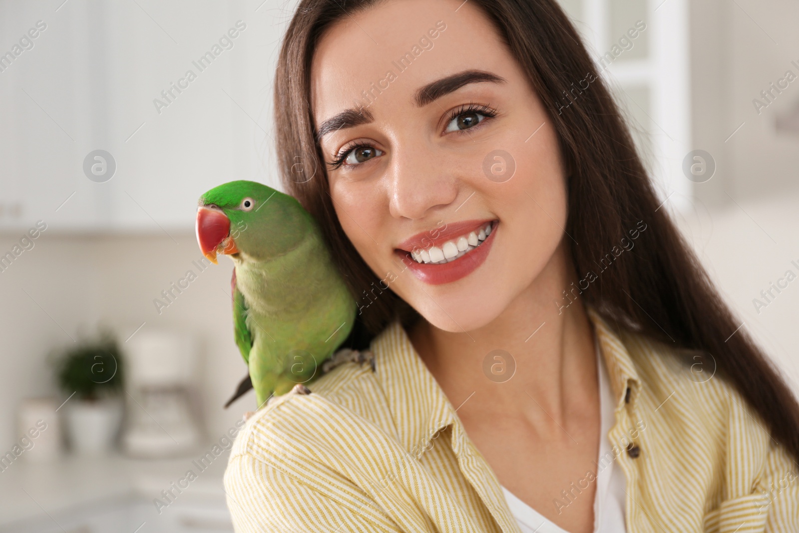 Photo of Young woman with Alexandrine parakeet indoors. Cute pet